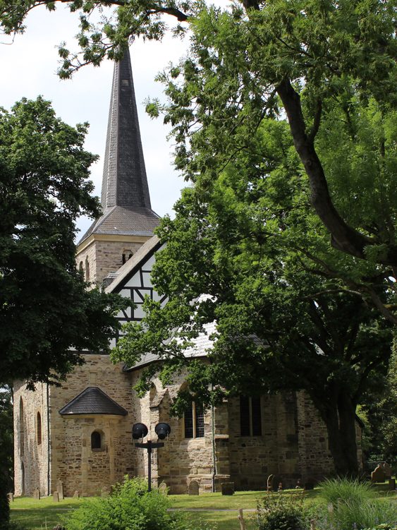 Historische Kirche mit spitzem Turm, umgeben von Bäumen und grünem Gelände.
Dorfkirche Stiepel in Bochum